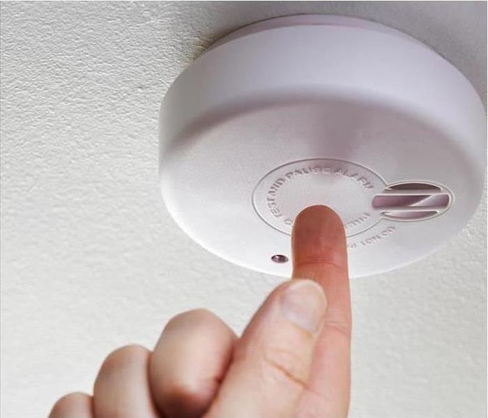A hand reaches to test a smoke detector